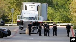 San Antonio police officers investigate the scene Sunday, July 23, 2017, where eight people were found dead in a tractor-trailer loaded with at least 30 others outside a Walmart store in stifling summer heat in what police are calling a horrific human tra