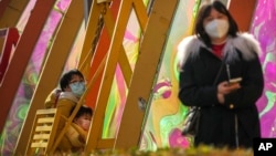 Žena i dete pored ljuljaške ispred ponovo otvorenog tržnog centra u Pekingu, 7. decembar 2022. 