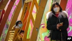 A woman and a child wearing face masks ride on a swing outside a reopened shopping mall after authorities started easing some of the anti-virus controls in Beijing, Dec. 7, 2022. 