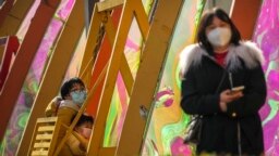 Una mujer y un niño con mascarillas se montan en un columpio frente a un centro comercial reabierto después de que las autoridades comenzaran a flexibilizar algunos de los controles antivirus en Beijing, el 7 de diciembre de 2022.