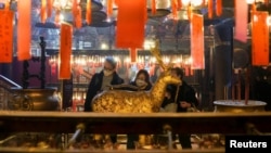 Jemaah yang mengenakan masker berdoa dan menyentuh rusa emas pada Malam Tahun Baru Imlek, di Kuil Man Mo di Hong Kong, China, 31 Januari 2022. (Foto: REUTERS/Lam Yik)