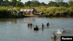 FILE - Refugees, who have fled a flare-up in fighting between the Myanmar army and insurgent groups and settled temporarily on the Moei River Bank, cross the river to receive aid from Thailand on the Thai-Myanmar border, in Mae Sot, Thailand, Jan. 7, 2022