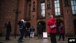 FILE - People wait for their turn to enter Stockholm's City Hall that temporarily served as a COVID-19 vaccination site, in Stockholm, Sweden, Feb. 21, 2021. 