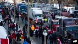 FILE - People walk past parked trucks on Wellington Street during a demonstration against COVID-19 restrictions at Parliament House in Ottawa, Canada, on Jan. 29, 2022.