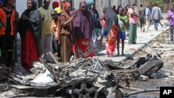 Somalis stand over the wreckage of car bomb which exploded outside a restaurant in Mogadishu, Somalia, April , 21, 2015.