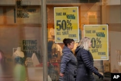 Pedestrians pass signs in the window of an Urban Outfitters store advertising a sale, in downtown Seattle, Jan. 31, 2022.