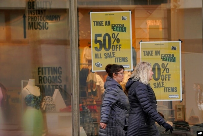 Pedestrians pass signs in the window of an Urban Outfitters store advertising a sale, in downtown Seattle, Jan. 31, 2022.