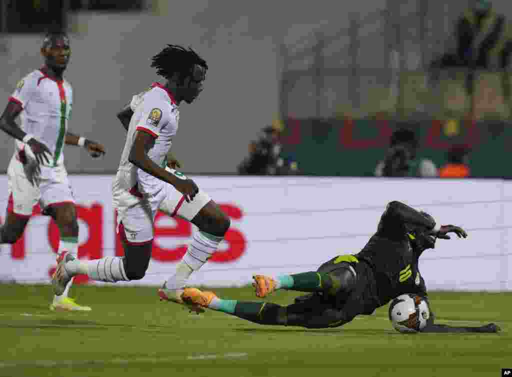 Senegal&#39;s Sadio Mane, right, falls down after a challenge from Burkina Faso&#39;s Issa Kabore, middle, in Cameroon, Feb. 2, 2022.