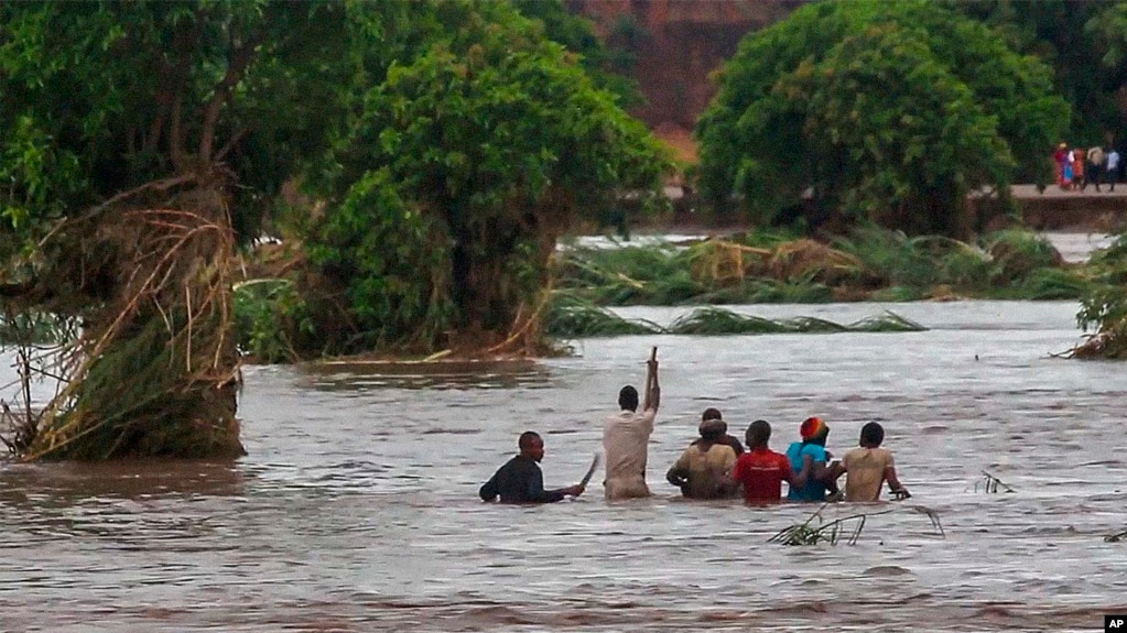In this image made from video, people walk on a road swept by flooding waters in Chikwawa, Malawi, Jan. 25, 2022.