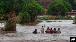 In this image made from video, people walk on a road swept by flooding waters in Chikwawa, Malawi, Jan. 25, 2022.