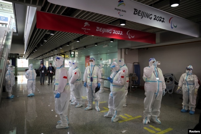 People wearing personal protective equipment (PPE), designed to prevent the spread of the coronavirus disease (COVID-19), stand inside Beijing Capital International Airport ahead of the Beijing 2022 Winter Olympics in Beijing, China January 31, 2022. (REUTERS/Phil Noble)