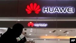 FILE - A man lights a cigarette outside a Huawei retail shop in Beijing, Dec. 6, 2018. 