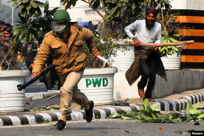 Seorang petani mengejar seorang petugas polisi selama protes terhadap undang-undang pertanian yang diperkenalkan oleh pemerintah, di New Delhi, India. (Foto: Reuters)