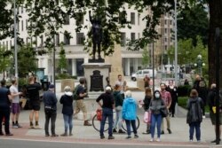 FILE - People look at a statue of a Black Lives Matter protester by British artist Marc Quinn erected in the spot once occupied by the statue of a slave trader in the English city of Bristol, July 15, 2020.