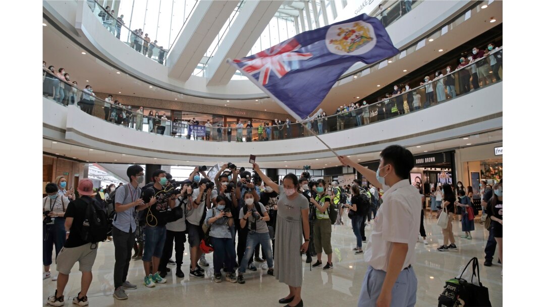 Protesters hold a British National (Overseas) passport and Hong Kong colonial flag in a shopping mall during a protest against China's national security legislation for the city, in Hong Kong, Friday, May 29, 2020.