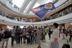 Protesters hold a British National (Overseas) passport and Hong Kong colonial flag in a shopping mall during a protest against China's national security legislation for the city, in Hong Kong, Friday, May 29, 2020.