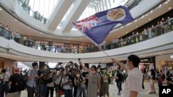 Protesters hold a British National (Overseas) passport and Hong Kong colonial flag in a shopping mall during a protest against China's national security legislation for the city, in Hong Kong, Friday, May 29, 2020.