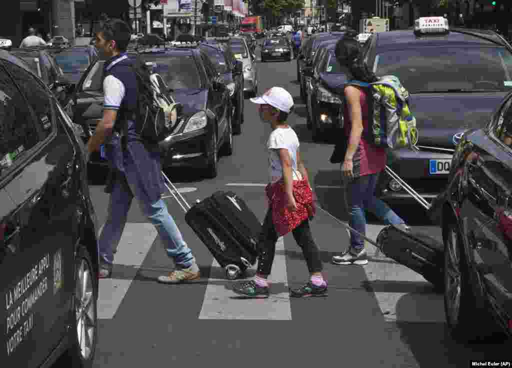Des touristes marchant à pieds, passent, bagages mains, des taxis bloquant une avenue lors d'une manifestation de chauffeurs de taxi à Paris, France, le 25 juin, 2015. 