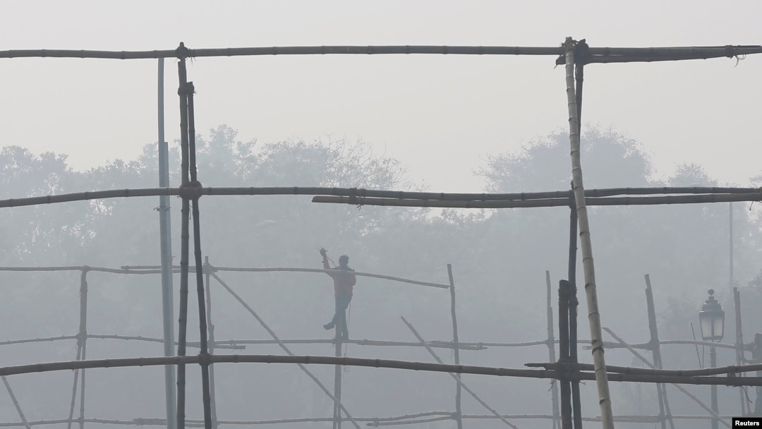FILE - A laborer dismantles scaffolding near the India Gate war memorial on a smoggy day in New Delhi.