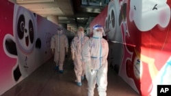 FILE - Workers wearing protective gear walk through the airport ahead of the 2022 Winter Olympics, Feb. 1, 2022, in Beijing.