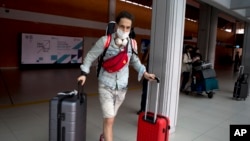A Russian tourist carries his luggage upon his arrival at Bali's international airport, Indonesia on Friday, Feb. 4, 2022. (AP Photo/Firdia Lisnawati)