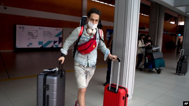 A Russian tourist carries his luggage upon his arrival at Bali's international airport, Indonesia on Friday, Feb. 4, 2022. (AP Photo/Firdia Lisnawati)