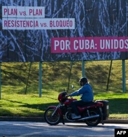 A man rides his motorcycle near a banner reading 'Plan vs. plan. Resistance vs. blockade. For Cuba: United' in Havana, on Feb. 4, 2022.