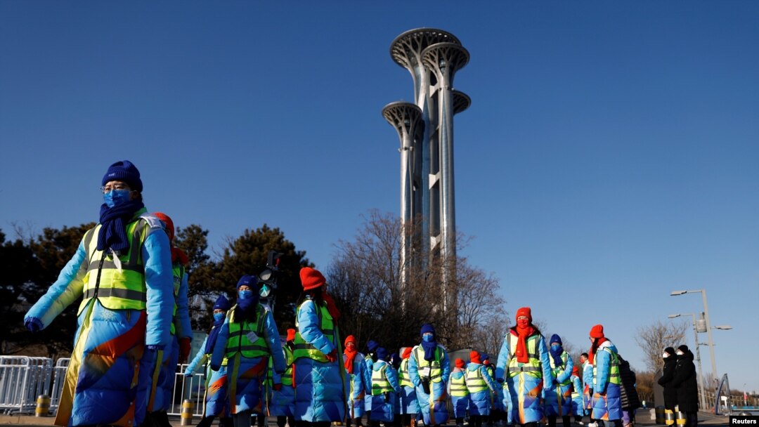 Para sukarelawan berjalan melewati Menara Olimpiade dekat Stadion Nasional, tempat berlangsungnya upacara pembukaan Olimpiade Musim Dingin Beijing 2022, di Beijing, China, 4 Februari 2022. REUTERS/Carlos Garcia Rawlins