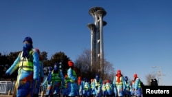 Para sukarelawan berjalan melewati Menara Olimpiade dekat Stadion Nasional, tempat berlangsungnya upacara pembukaan Olimpiade Musim Dingin Beijing 2022, di Beijing, China, 4 Februari 2022. REUTERS/Carlos Garcia Rawlins