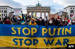 FILE - Demonstrators hold a banner in the colors of the Ukrainian flag reading "Stop Putin, Stop war" during a protest at Berlin's Brandenburg Gate, Jan. 30, 2022.