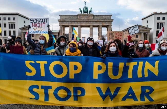 FILE - Demonstrators hold a banner in the colors of the Ukrainian flag reading "Stop Putin, Stop war" during a protest at Berlin's Brandenburg Gate, Jan. 30, 2022.