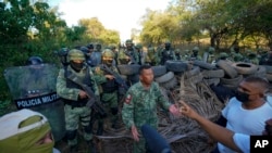 FILE - Residents who are fed up with the army’s strategy of simply separating the Jalisco and the Michoacan-based Viagras gangs, confront Mexican soldiers taking cover behind a barricade of car tires, in Loma Blanca, Mexico, Tuesday, Nov. 16, 2021.