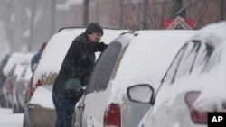 A motorist cleans his vehicle of snow, Feb. 3, 2022, in Indianapolis. A storm is spreading rain, freezing rain and snow across the U.S.