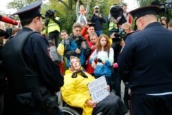 FILE - A wheelchair-bound woman activist surrounded by journalists holds a poster reading, "The Constitution breakers to be brought to justice!" as she talks to police officers during a protest in the center of Moscow, Aug. 17, 2019.