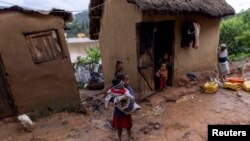 Seorang anak perempuan memegang bayi di luar rumah yang hancur diterpa banjir saat saat Topan Batsirai melanda wilayah Fianarantsoa di Madagascar, pada 6 Februari 2022. (Foto: Reuters/Alkis Konstantinidis)