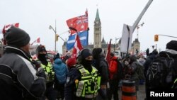 FILE - Police officers stand among protesters in front of Parliament Hill as truckers and their supporters continue to rally against COVID-19 restrictions and vaccine mandates, in Ottawa, Canada, Feb. 6, 2022.