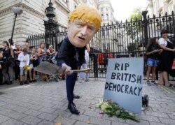A man with a giant Boris Johnson 'head' pretends to dig a grave at the foot of a symbolic tombstone outside Downing Street in London, England, Aug. 28, 2019.