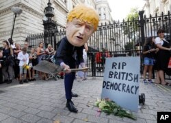 A man with a giant Boris Johnson 'head' pretends to dig a grave at the foot of a symbolic tombstone outside Downing Street in London, England, Aug. 28, 2019.