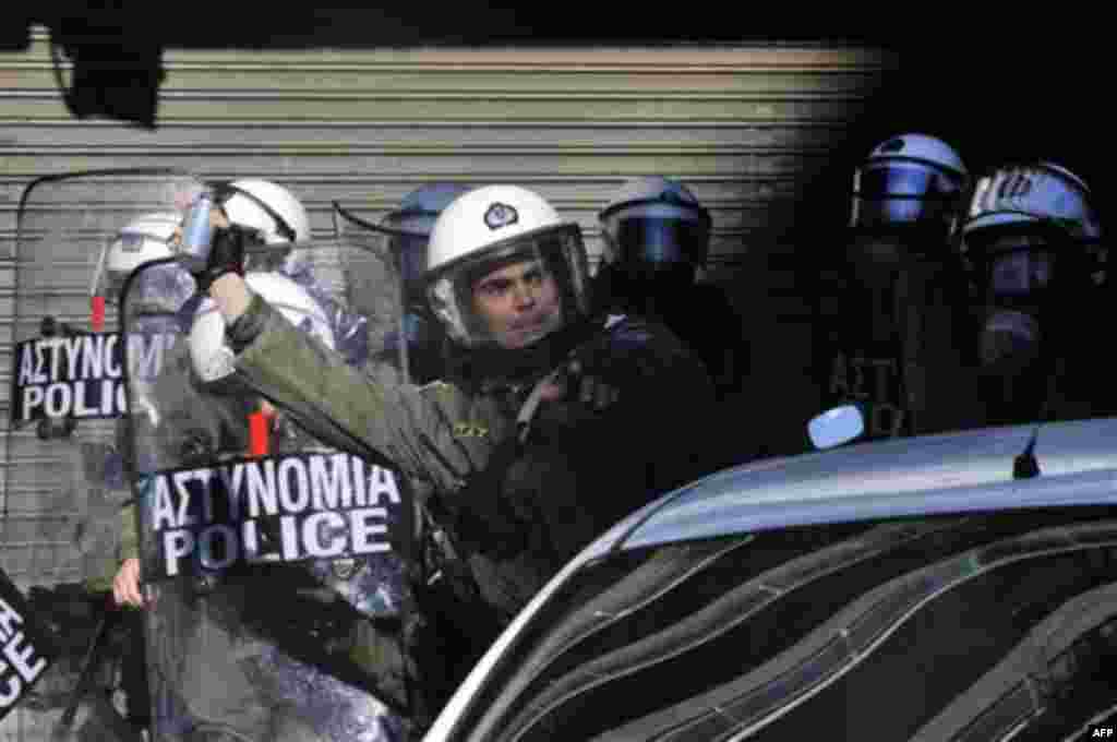 A riot police officer throws a flash grenade to protesters during clashes in northern port city of Thessaloniki, Greece, Wednesday, Dec. 15, 2010. Protesters clashed with riot police across Athens on Wednesday, torching cars, hurling gasoline bombs and se