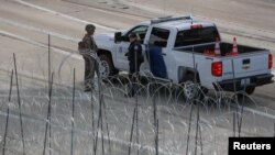 Un militar de EE.UU. habla con un agente de aduanas en el cruce de San Ysidro, California, delante de una valla alambrada.