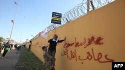 ARCHIVO- Un miembro de un grupo paramilitar chiíta iraquí ayuda a un manifestante que sostiene un cartel que denuncia a EE.UU. a trepar el muro exterior de la Embajada de EE.UU. en la Zona Verde de Bagdad. Dic. 31, 2019.