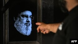 A man points to a television set displaying an image of the late leader of Hezbollah Hassan Nasrallah with a black stripe for mourning during a broadcast from the private Lebanese station NBN in Beirut on September 28, 2024.