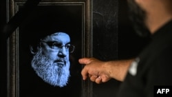 A man points to a television set displaying an image of the late leader of Hezbollah, Hassan Nasrallah, with a black stripe for mourning during a broadcast from the private Lebanese station NBN in Beirut, Sept. 28, 2024.