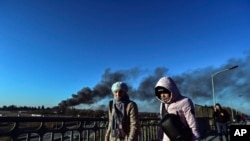 人们走过一座乌克兰西部城市利沃夫的一座立交桥，背后是从遭到俄罗斯导弹袭击的机场附近冒出的浓烟。(2022年3月18日)