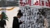 FILE - An anti-government protester checks his mobile phone in front of a wall of graffiti in Arabic that reads, "I am the revolution leader," in downtown Beirut, Lebanon, Nov. 21, 2019. 