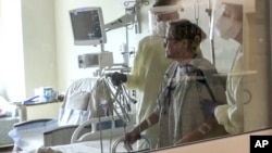 FILE - Coronavirus patient Joan Bronson walks across her hospital room with the help of a physical therapist at Ochsner Medical Center in the New Orleans suburb of Jefferson, La., Aug.11, 2021.