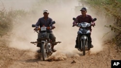 Cambodian farmers drive their motorbike through a dirt road at a remote rural area as they head to work in their farm, near Russey Chroy village, Kandal province, north of Phnom Penh, Cambodia, Tuesday, March 31, 2015. (AP Photo/Heng Sinith)