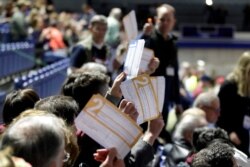 Caucus goers seated in the section for Democratic presidential candidate former Vice President Joe Biden hold up their first votes as they are counted at the Knapp Center on the Drake University campus in Des Moines, Iowa, Feb. 3, 2020.