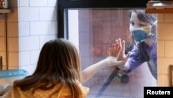 FILE - Friends say hello through a kitchen window during the outbreak of the coronavirus disease in Brooklyn, New York, May 17, 2020.