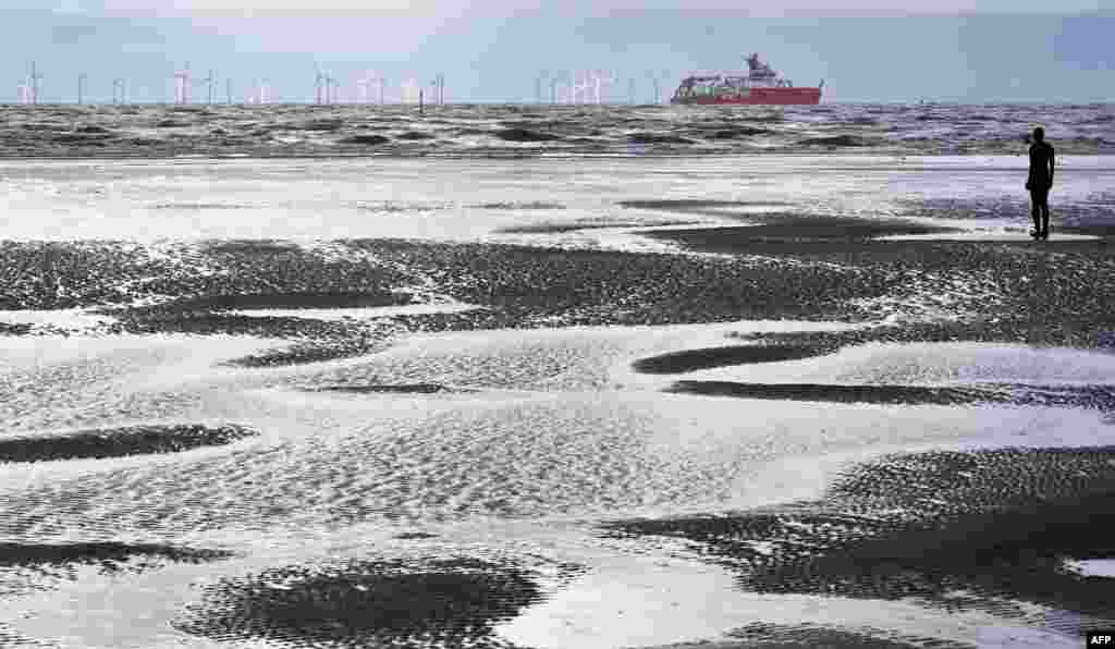 Polar research ship, the RRS Sir David Attenborough, sails out of the Mersey River and past Antony Gormley's art installation, '"Another Place," at Crosby, England.
